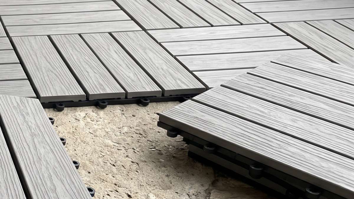 Close-up of gray interlocking WPC composite deck tiles being installed on a concrete surface showing the click-and-lock plastic grid base
